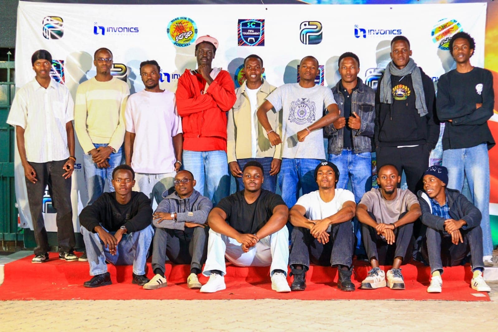 Guests and organisers posed in rows on a red-carpeted stage in front of a branded backdrop